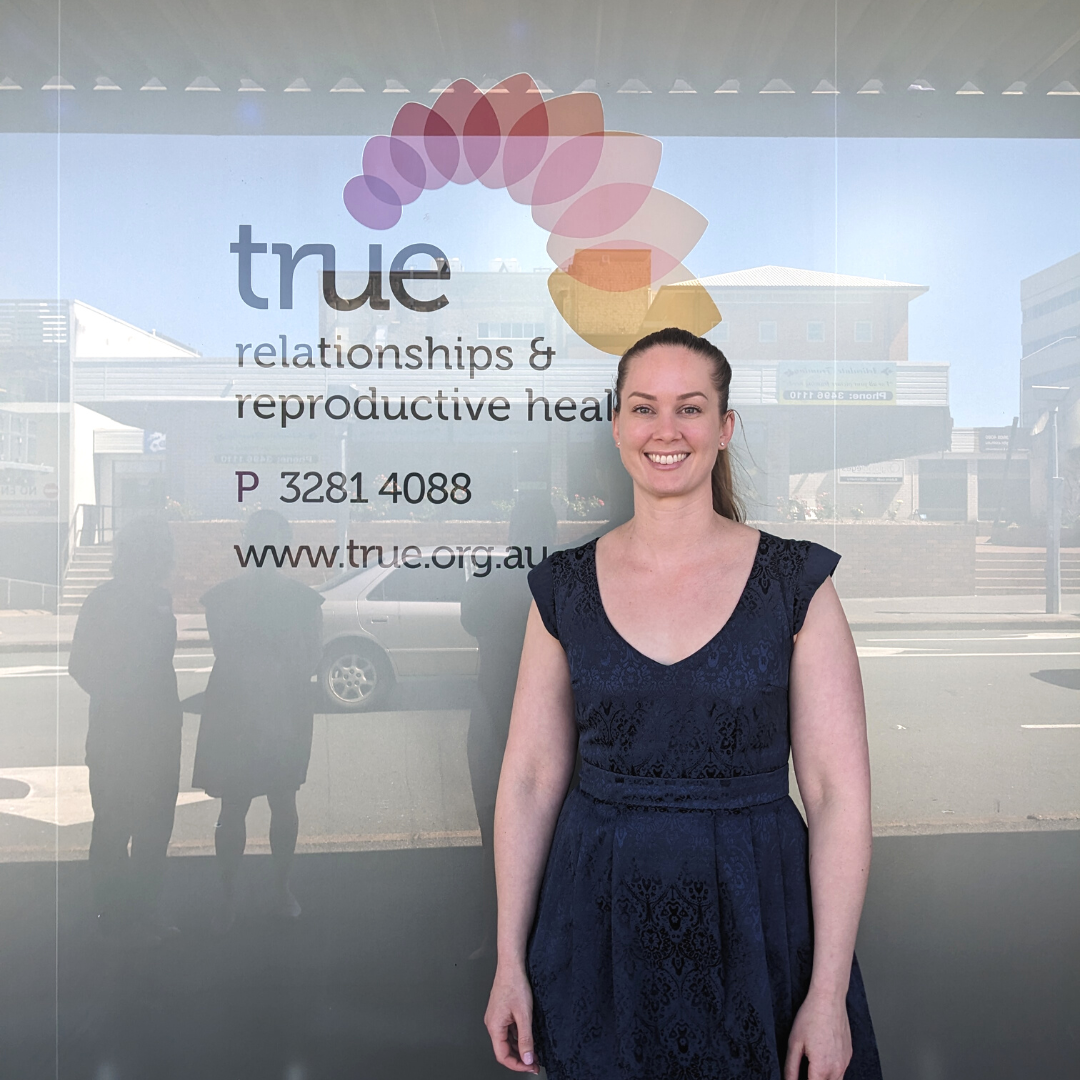 A photo of Dr Angela Smith in front of the Ipswich clinic window with the True Logo on the wall.