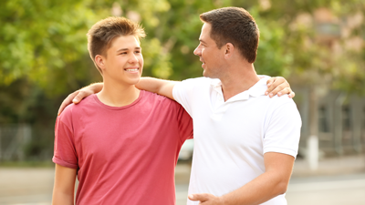 Father and son smiling with arms around each other\